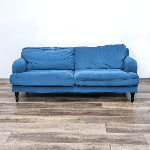 Blue fabric sofa with rounded arms and spindle legs on wooden floor.  