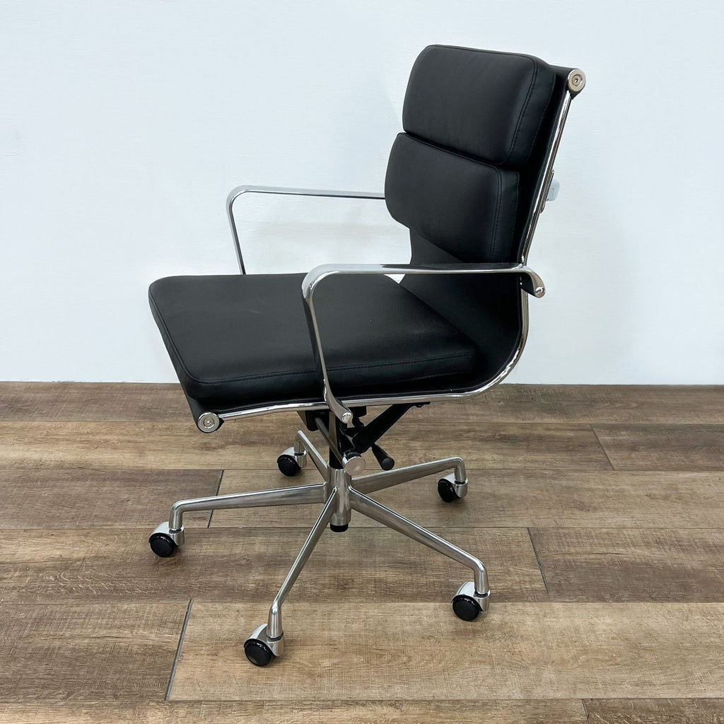 Side view of a black cushioned chair with a sleek aluminum frame and wheels on a wooden surface.