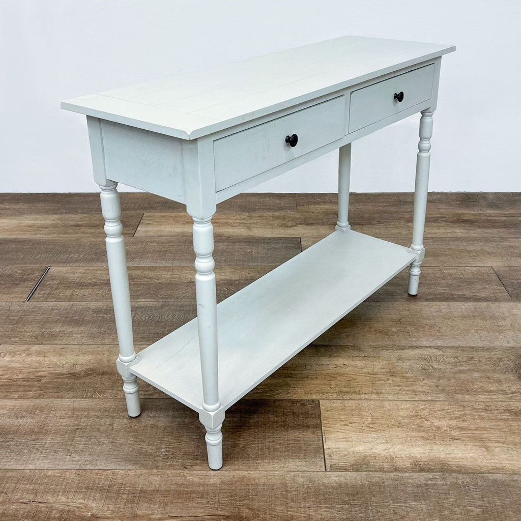 Angled view of a white console table with two black-knobbed drawers and a storage shelf below.