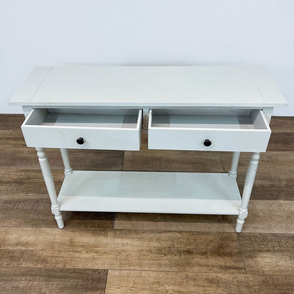 Top view of a white console table with two open drawers and a bottom shelf on wooden flooring.