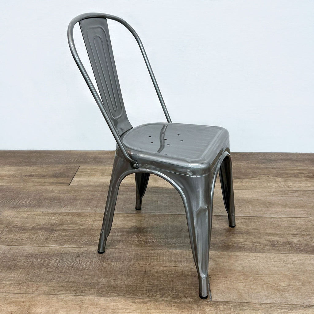 Side view of a compact, stackable metal chair with a curved back and tapered legs.