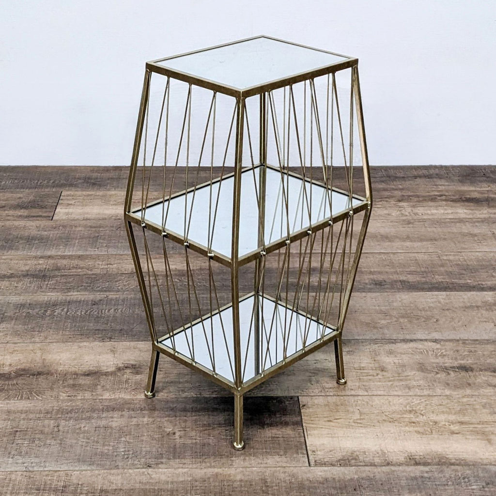 Golden wireframe side table with three glass shelves on a wooden floor.
