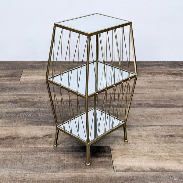 Golden wireframe side table with three glass shelves on a wooden floor.