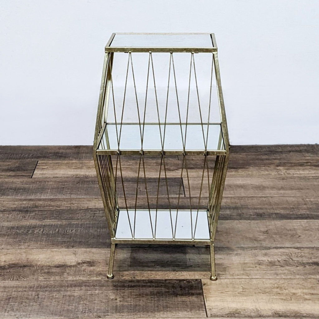 Stylish three-tier glass and brass display stand featuring a unique angular frame on wood flooring.