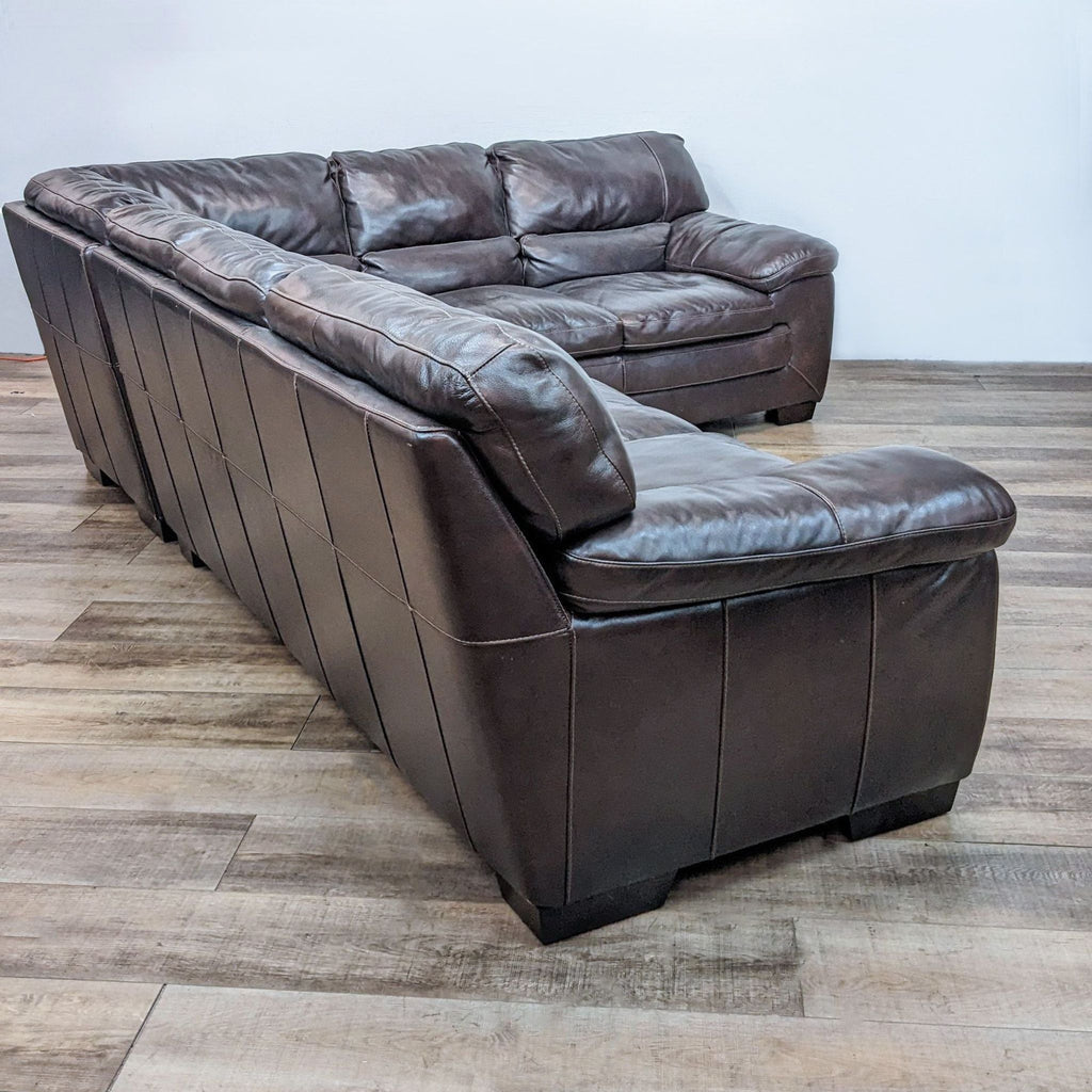 Back view of large brown leather sectional highlighting its sturdy design and dark finish block feet.