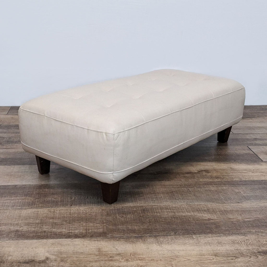 Rectangular leather ottoman showcasing dark finish legs and a minimalist design.