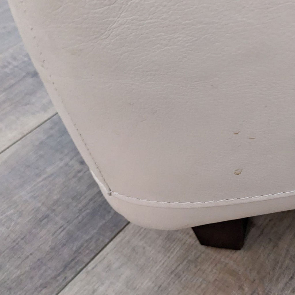 Close-up of the leather ottoman corner, highlighting stitching and leg details.