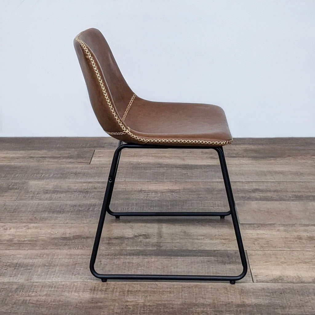 Side view of a contemporary dining chair featuring brown faux leather and a sturdy metal base.