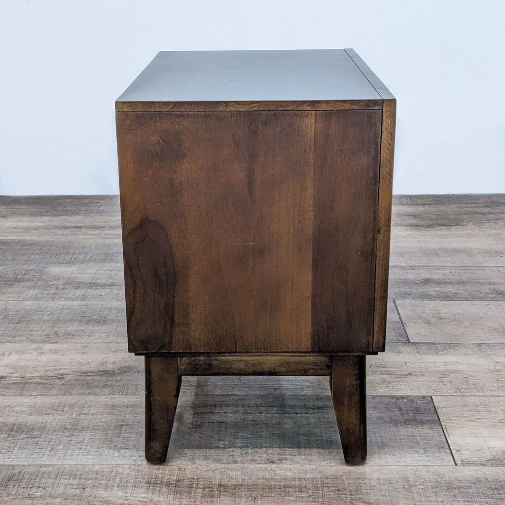 Side view of a wooden end table with simple design on a wooden floor.