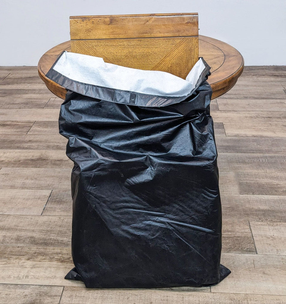 Round wooden table with a black bag containing an expansion leaf on top.