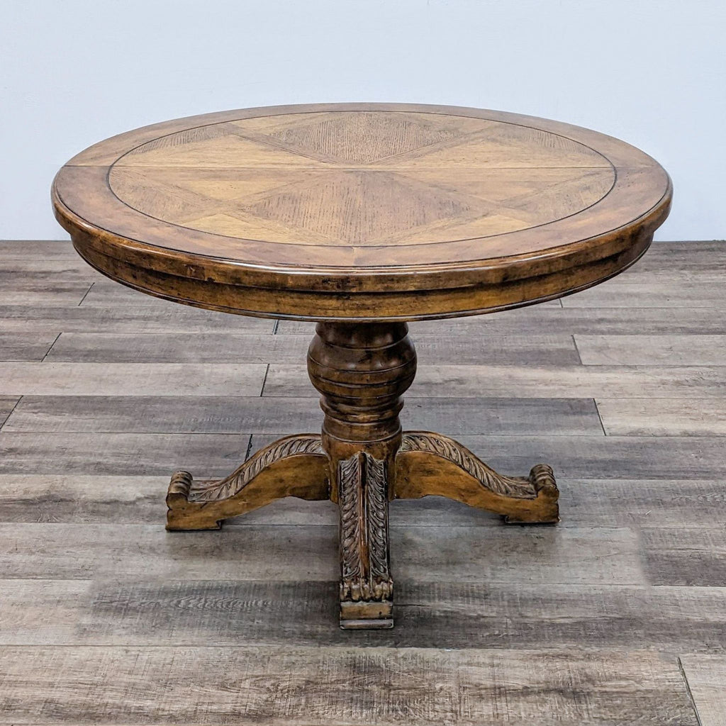 Round wooden dining table with ornate pedestal base on a hardwood floor.