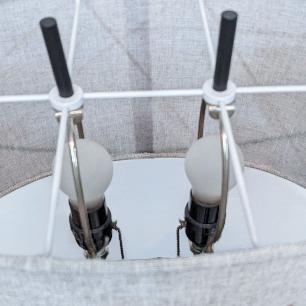 Close-up of dual light bulbs inside a gray lampshade with pull chains visible.
