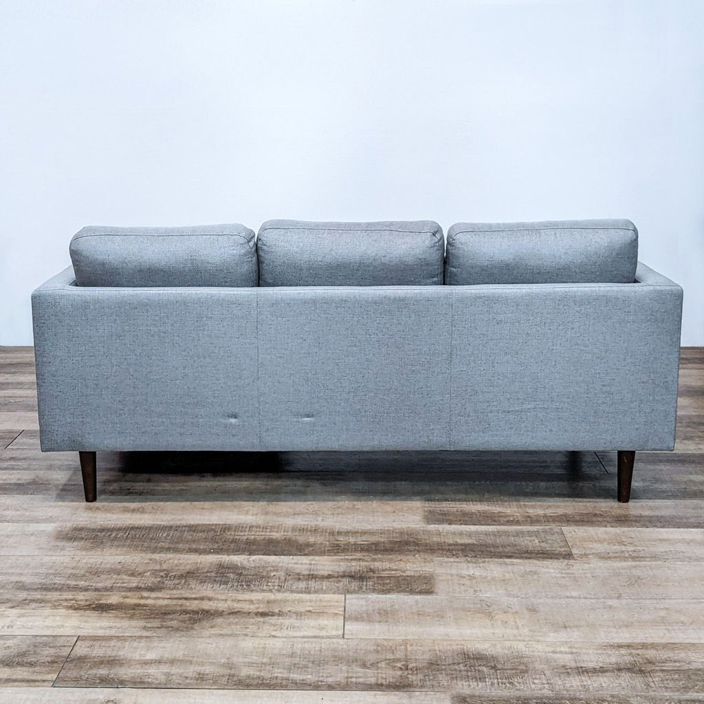 Rear view of gray fabric sectional with narrow arms and tapered wood feet.