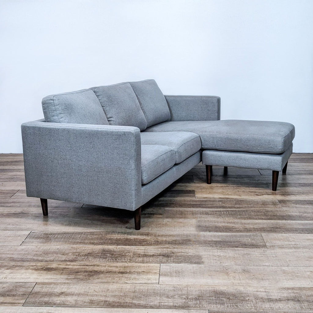Side view of gray sectional with reversible chaise, narrow arms, and tapered wood feet.