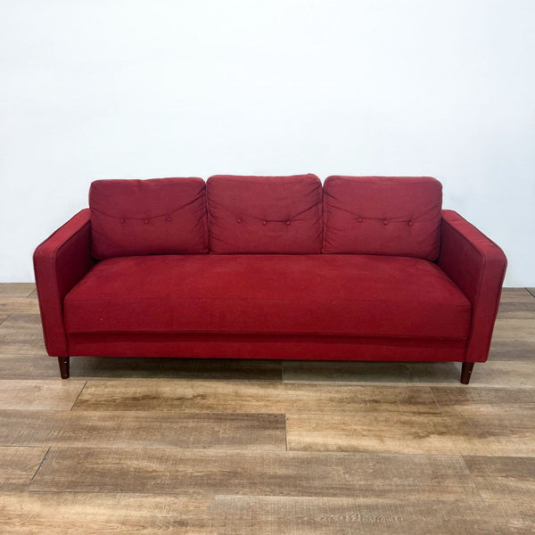Red sofa with three tufted back cushions and narrow arms on wood legs.