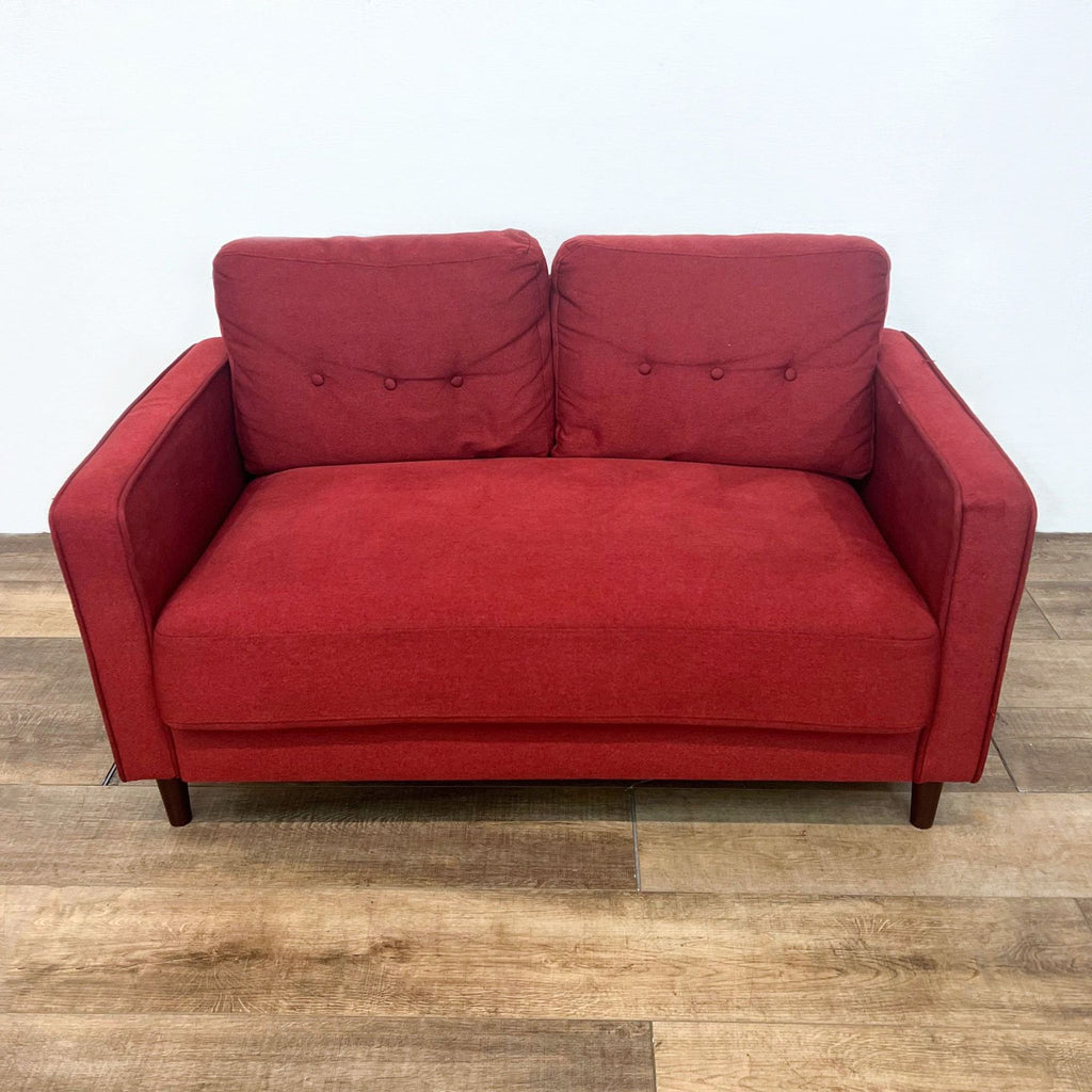 Red loveseat with tufted back cushions, narrow arms, and wooden tapered legs.