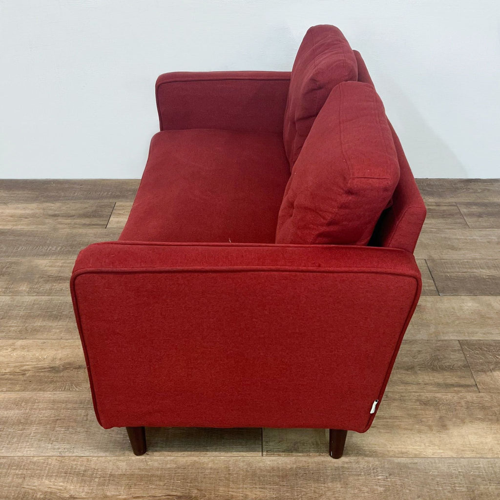 Side view of red loveseat highlighting narrow arms and wooden tapered legs.