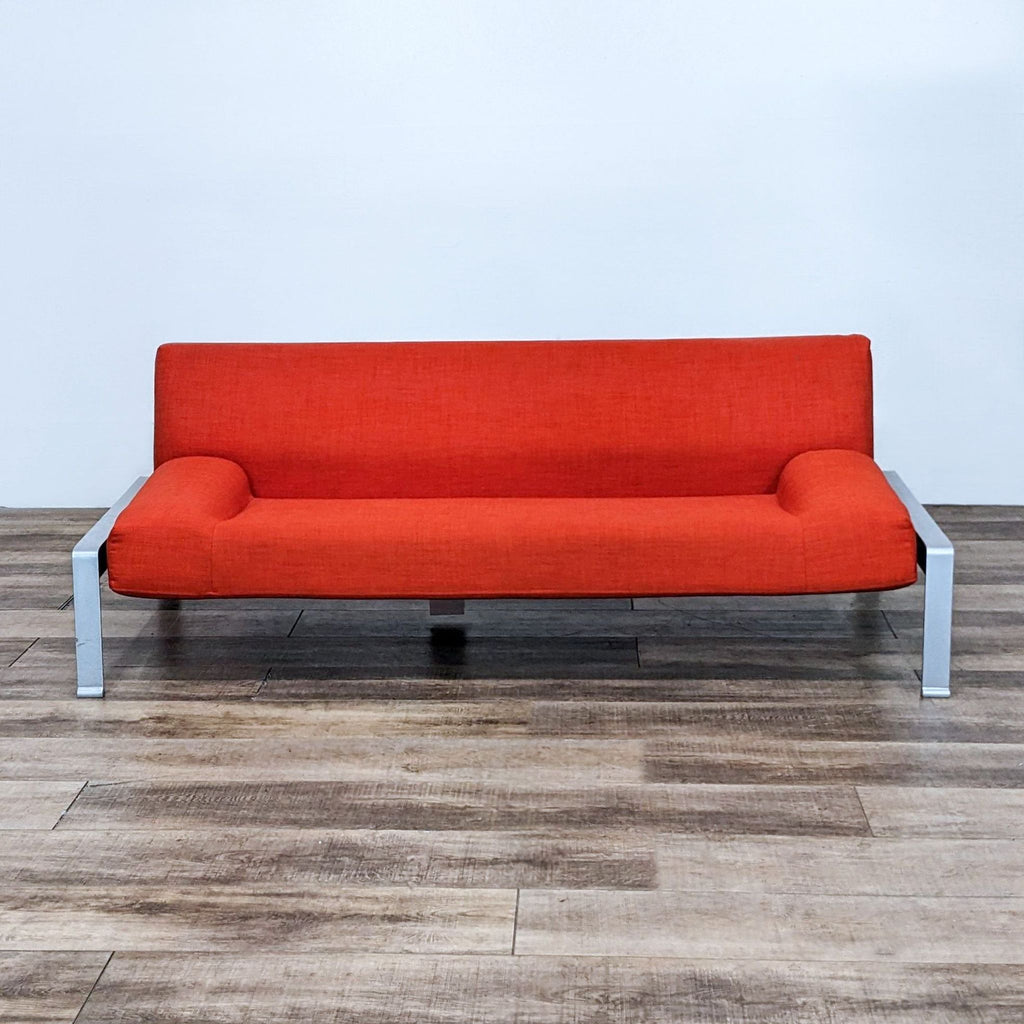 Modern red 3-seat sofa with low arms and a metal frame on wooden flooring.