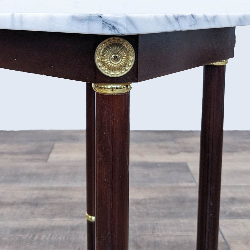 Close-up of brass detailing on Reperch end table with wooden legs and marble top.