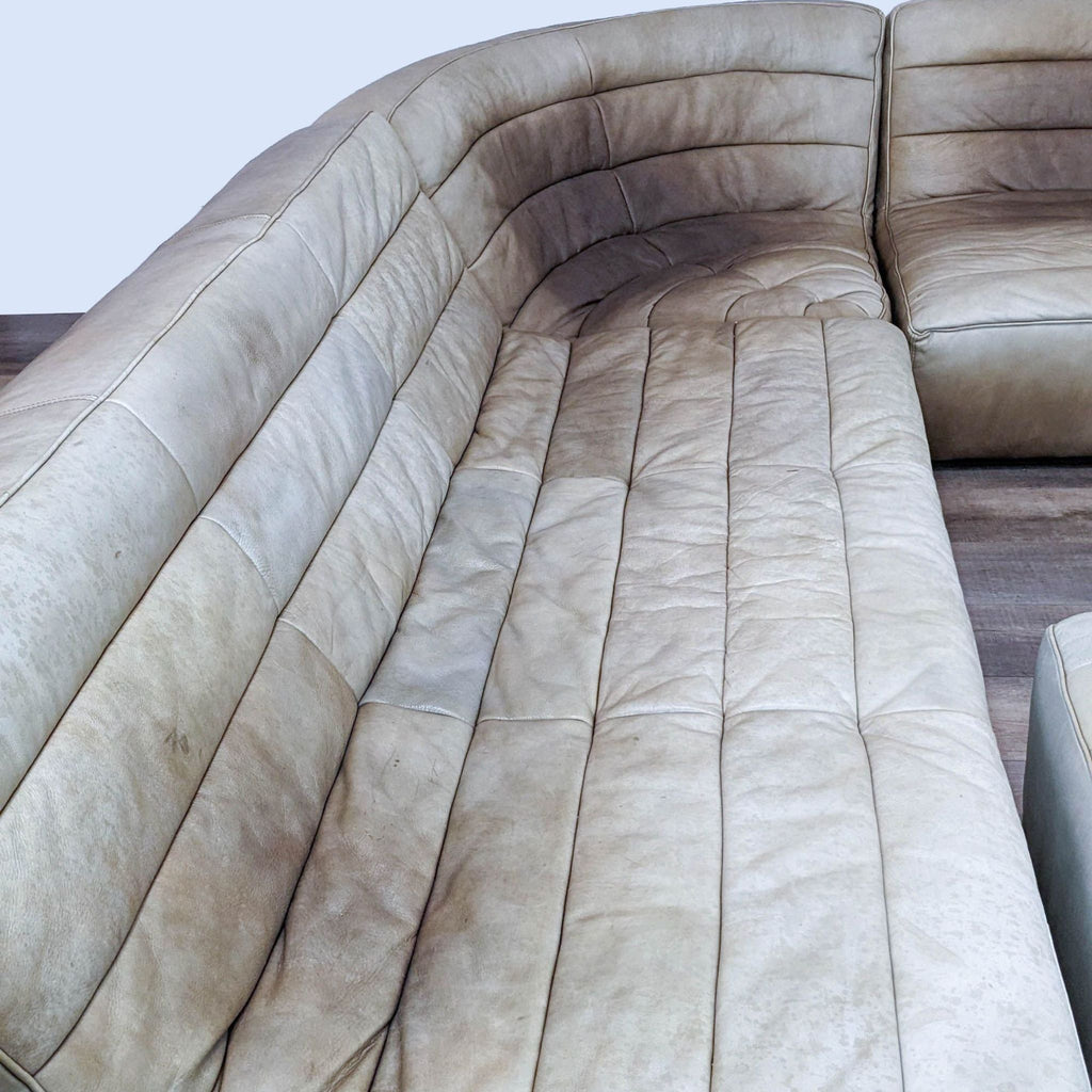Close-up of a vertically tufted leather sectional on wood floor.