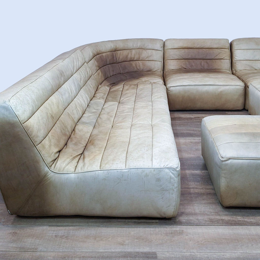 A modular sectional with worn tufted leather on wood flooring.