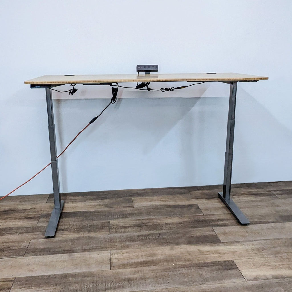 Adjustable height bamboo desk with white steel base, featuring a clamp-mounted surge protector.