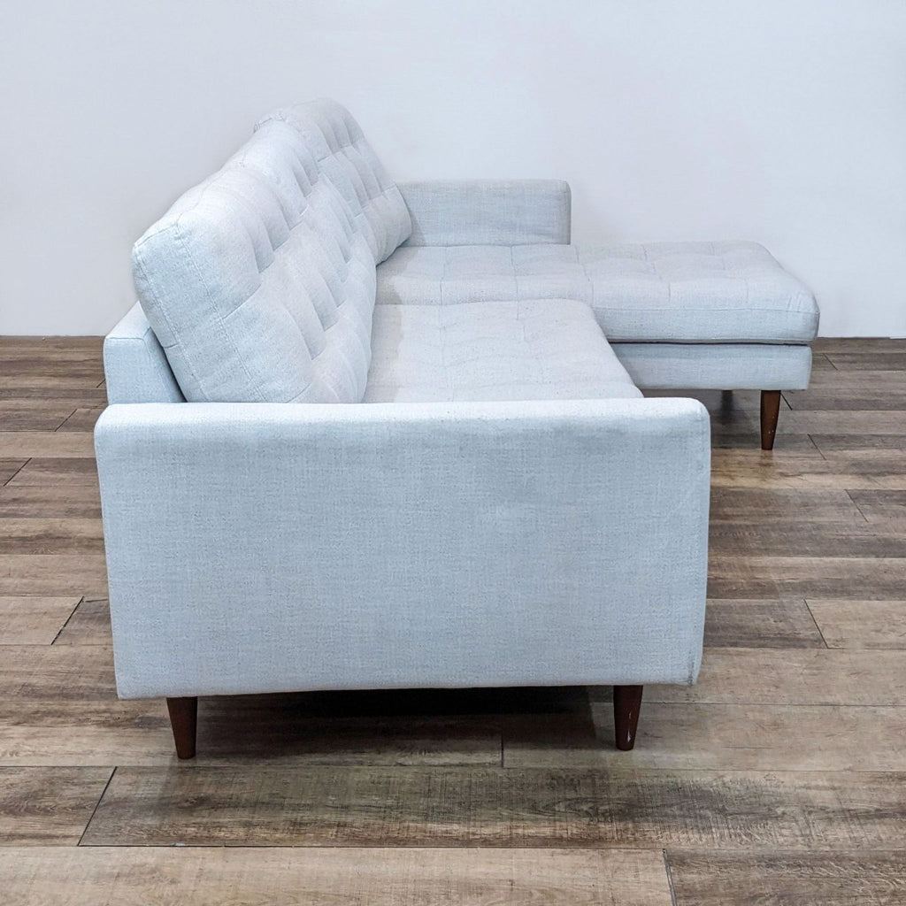 Side view of tufted sectional with sleek design and wooden legs.