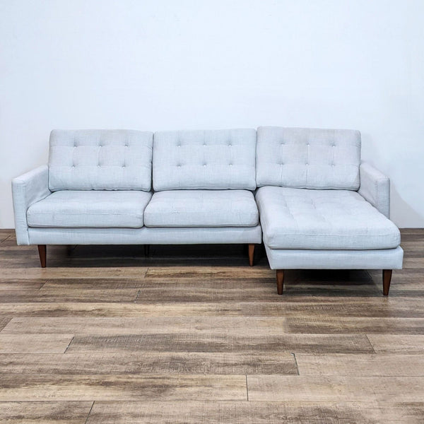 Tufted sectional with narrow arms and wood feet on wooden floor.