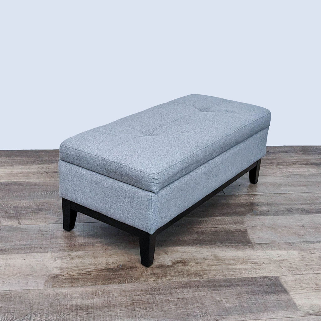Rectangular gray ottoman with tufted top, closed, dark legs.  