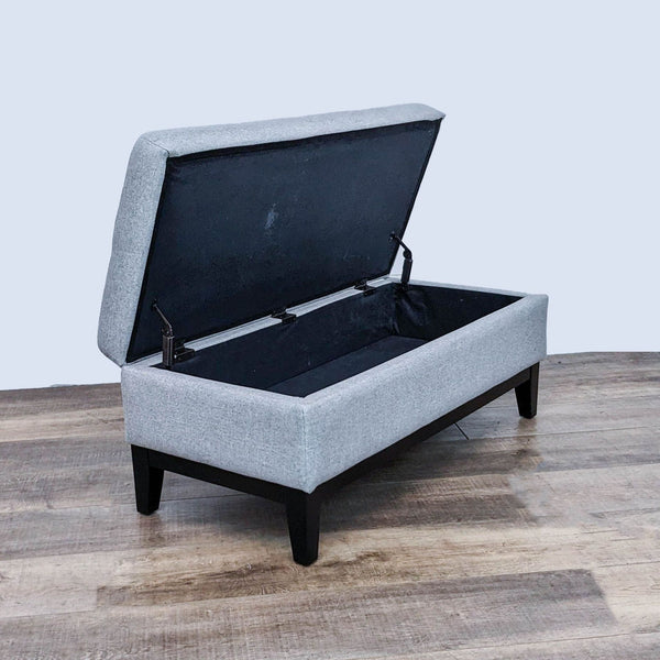 Gray fabric ottoman with tufted top and open storage, dark finish feet.  