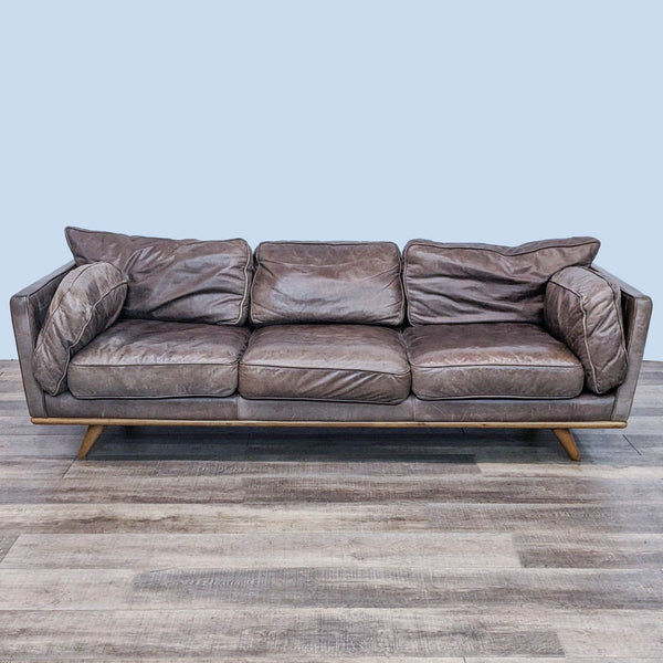 Mid-century brown leather sofa with cushion arms on a wooden frame.