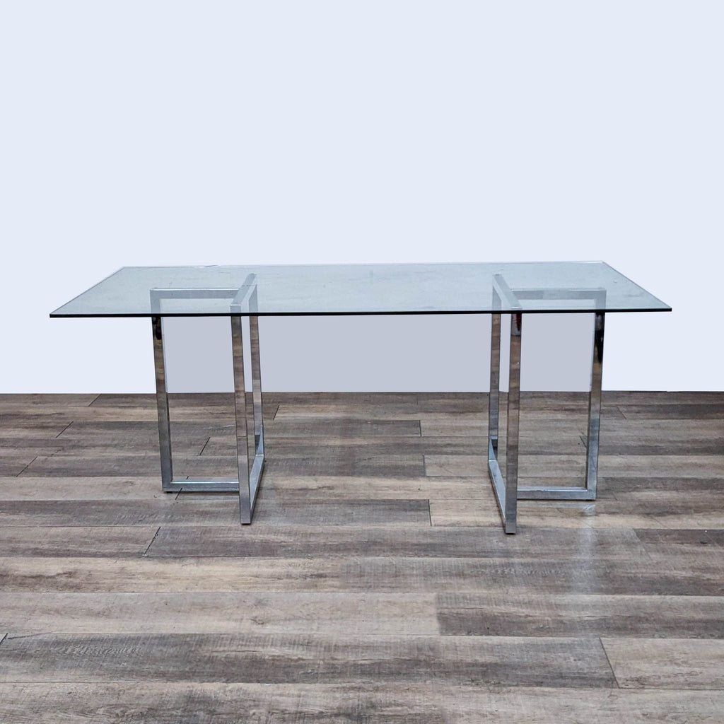 CB2 Silverado dining table with chrome base and glass top on wood floor.