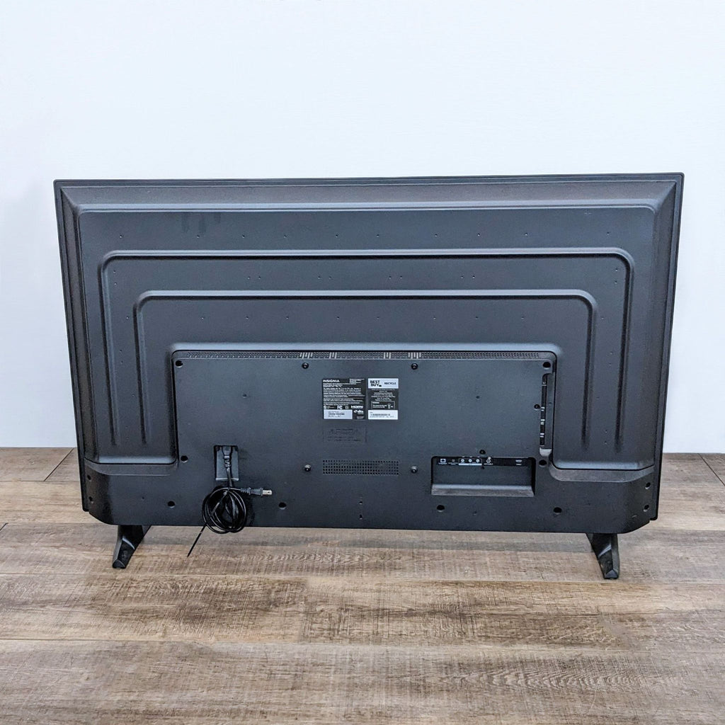 Back view of an Insignia Fire TV, revealing ports and cable connections on a wooden floor.