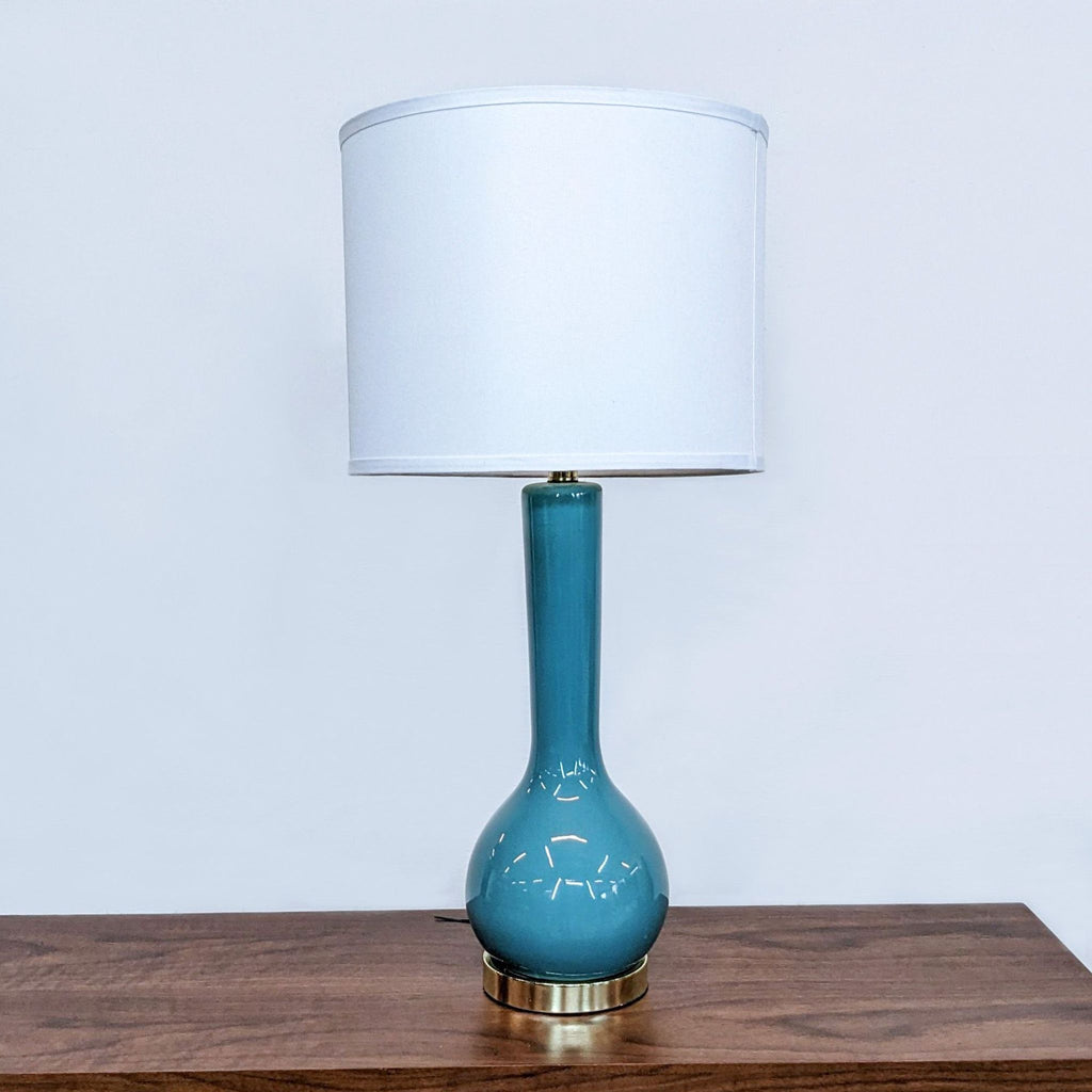 Tall teal lamp with white shade on a wooden surface.