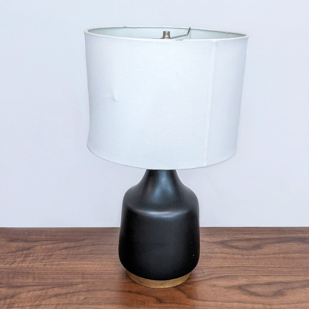Black ceramic table lamp with white shade on wooden surface.  