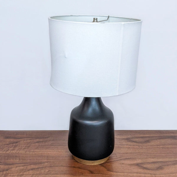 Black ceramic table lamp with white shade on wooden surface.  
