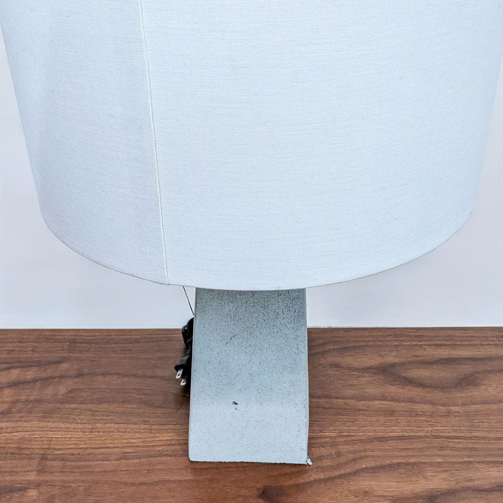 Side view of white cylindrical shade and rectangular concrete base on wooden surface.