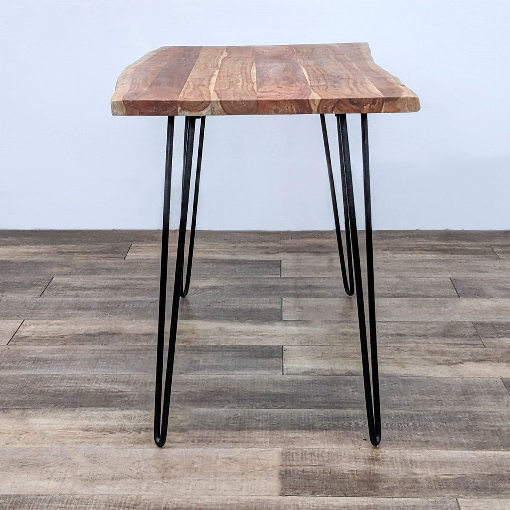 Counter height table with natural edge wood top and metal hairpin legs.