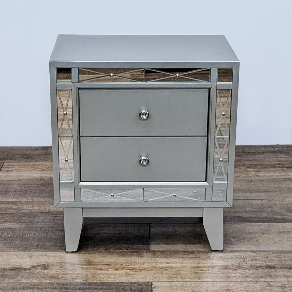 Metallic nightstand with two drawers and etched mirror panels, featuring tapered legs.