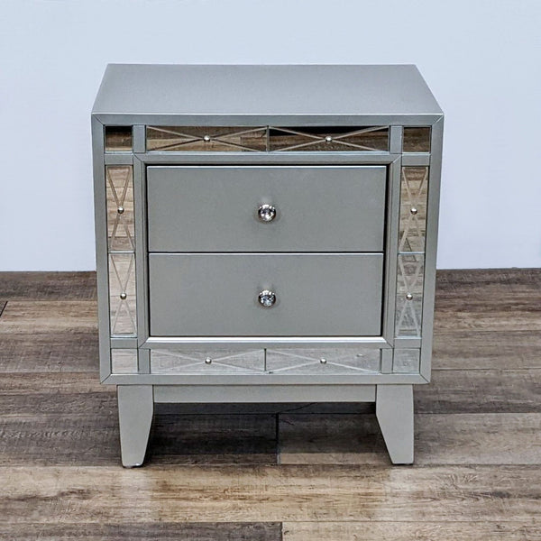 Metallic nightstand with two drawers and etched mirror panels, featuring tapered legs.