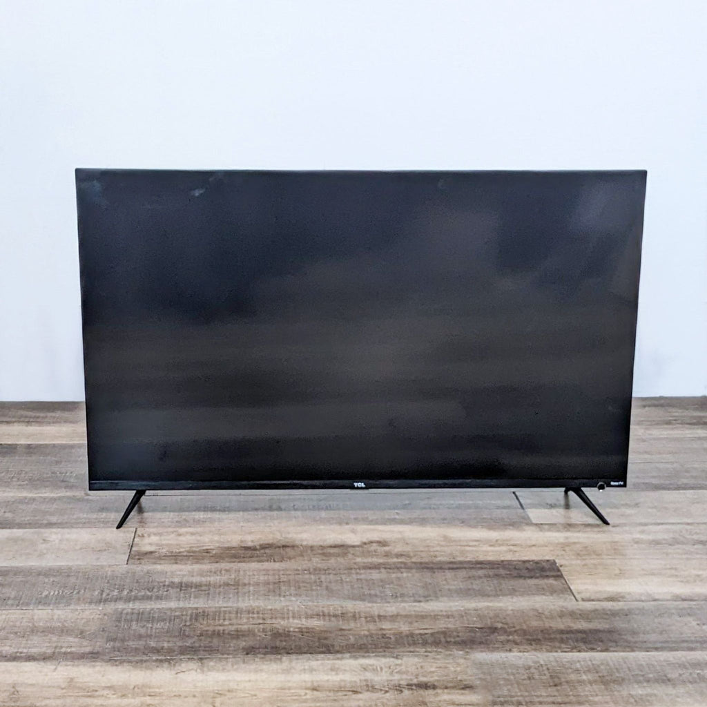 TCL 55-inch TV with a sleek, minimalistic design on a wooden floor.
