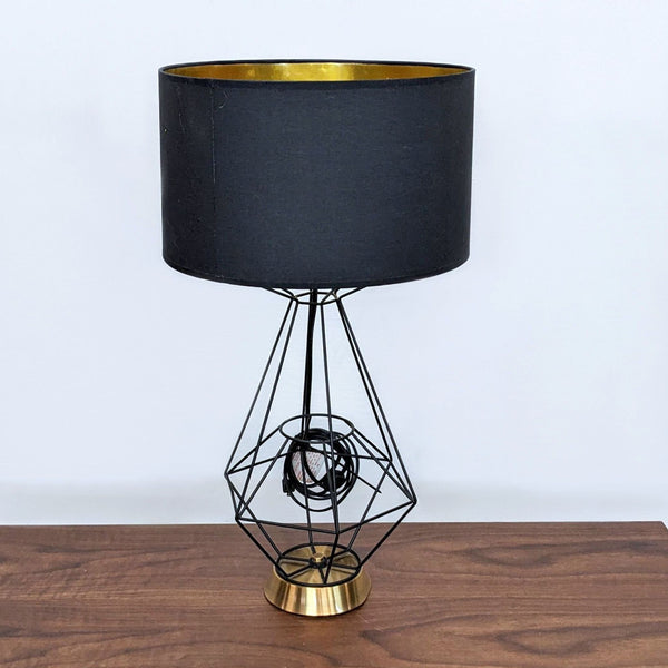 A black and gold lamp with a geometric wireframe design on a wooden surface.