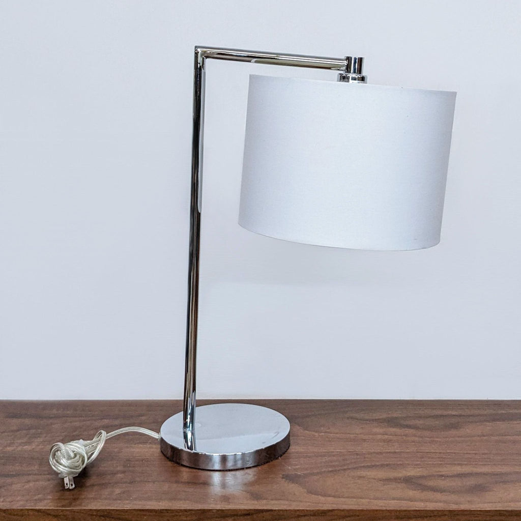 Reperch lamp with chrome base and white shade on a wooden surface.