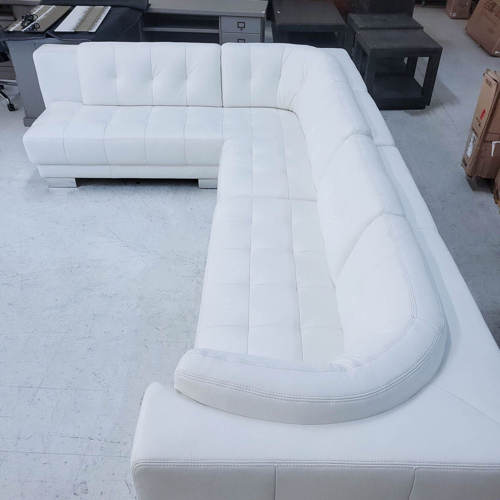 2. Angled shot of a spacious, modern white leather sectional sofa with tufted design and chrome legs.