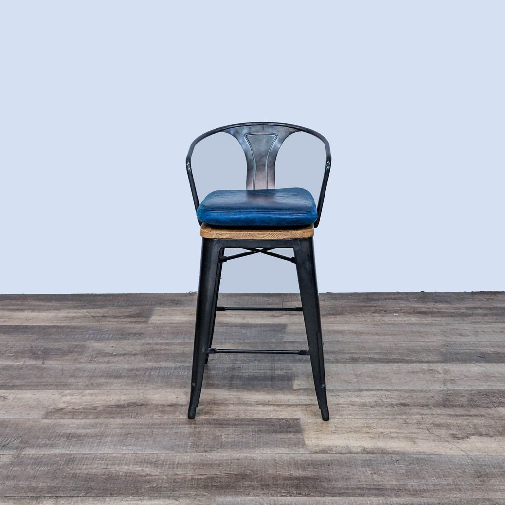 CB2 black metal frame barstool with solid wood seat and removable blue padded cushion on a wooden floor.
