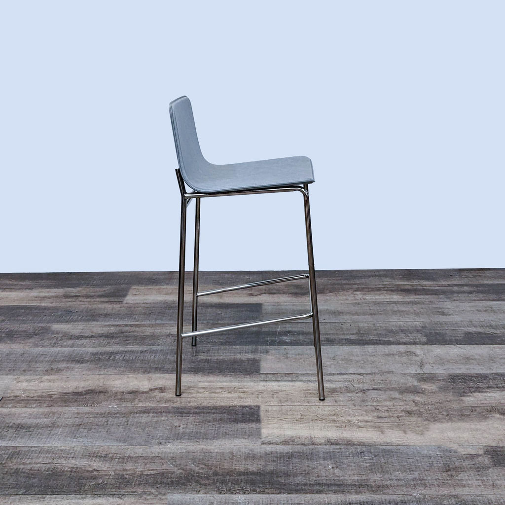 CB2 brand modern gray leather Strut barstool with chrome frame on a wooden floor.