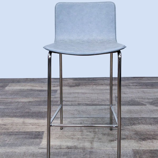 Modern gray leather CB2 Strut barstool with a sleek chrome frame, shown from the front against a wooden floor background.