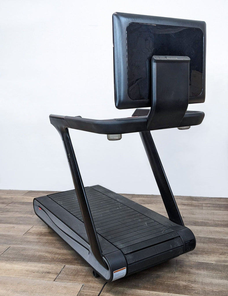 Side view of a Peloton treadmill with a large screen and sleek design on a wooden floor.