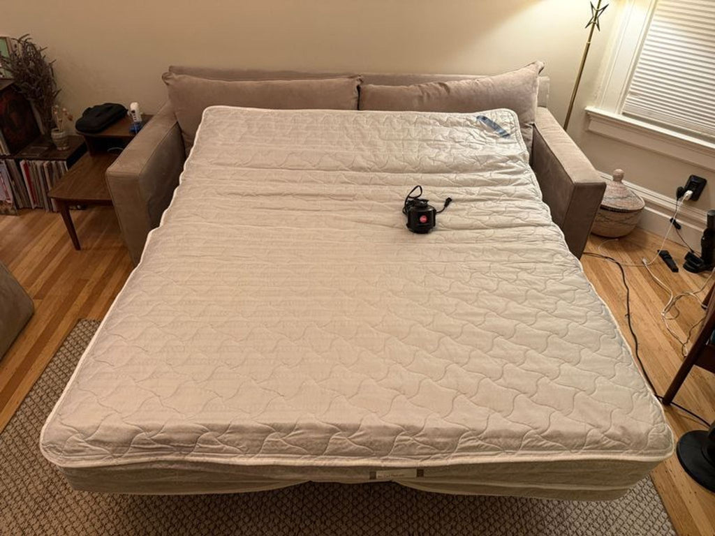 3. Room & Board sleeper sofa fully extended as a bed, showing a quilted mattress in a tidy living room setting.