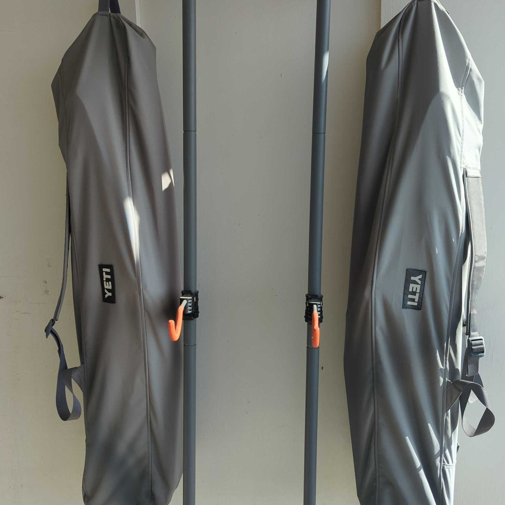 Two grey Yeti chair bags hanging upright by their straps, with poles and orange hooks visible between them.  